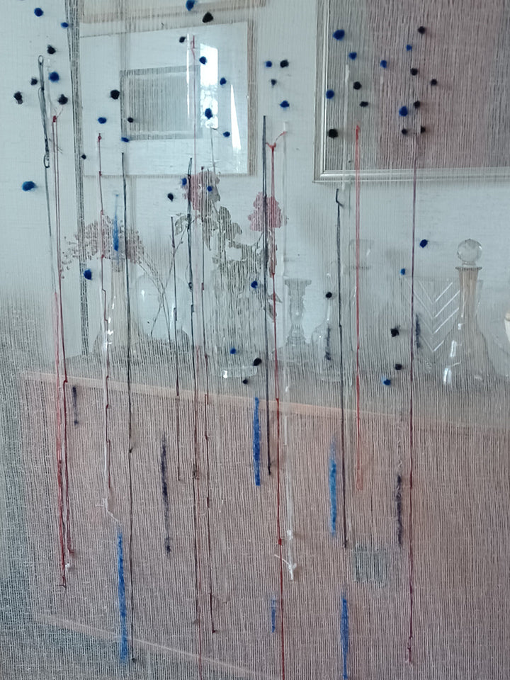 quadro con sfondo trasparente di tarlantana, con fili di lana e cotone che formano delle sottili forme astratte